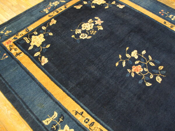 A plush dark navy rug with cream, pink, and blue floral motifs and a golden ochre border on wood floor.