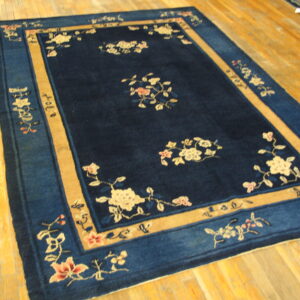 A blue rug with a broad tan border and scattered floral pattern rests on light plank wood flooring.