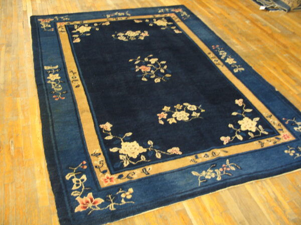 A blue rug with a broad tan border and scattered floral pattern rests on light plank wood flooring.