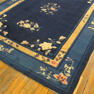 Floral navy and gold rug with wide borders lies on distressed light brown hardwood planks.