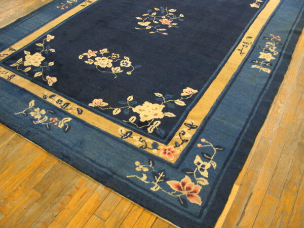 Floral navy and gold rug with wide borders lies on distressed light brown hardwood planks.
