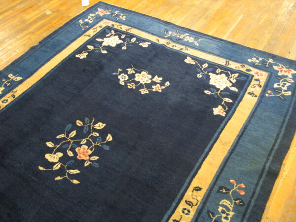 Low-pile navy blue rug with cream floral designs, framed by gold and light blue borders on polished wood planks.