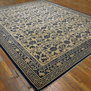 Tan rug with dense blue floral patterns and broad geometric fretwork borders on wood planks.
