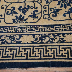 Tan and navy low pile rug featuring a scrolling floral field and detailed geometric border patterns.