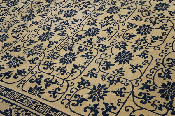 Navy blue floral motifs and vines cover a tan field, with a dark geometric border visible at the bottom.