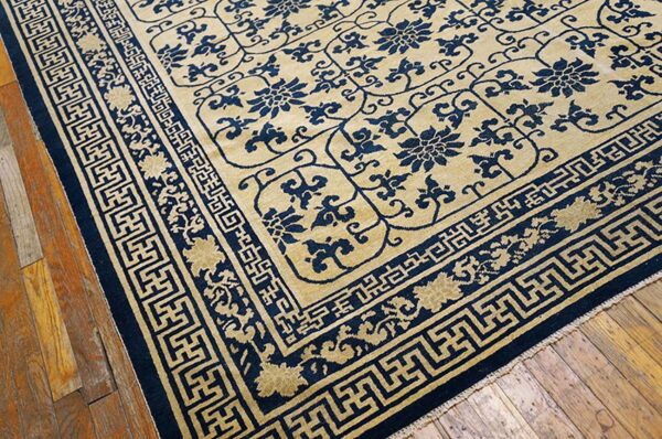A tan and navy rug with floral motifs and geometric borders rests on rustic hardwood floors.