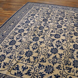 Beige rug featuring deep blue floral designs and geometric borders rests on plank wood flooring.