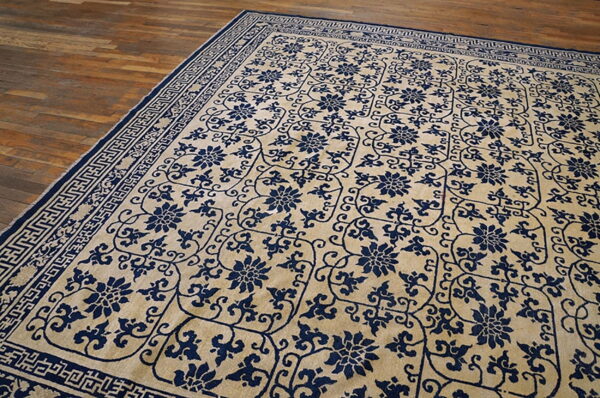 Beige rug featuring deep blue floral designs and geometric borders rests on plank wood flooring.