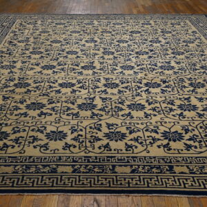 Beige rug featuring repeated navy blue floral motifs and complex geometric borders on a distressed hardwood floor.