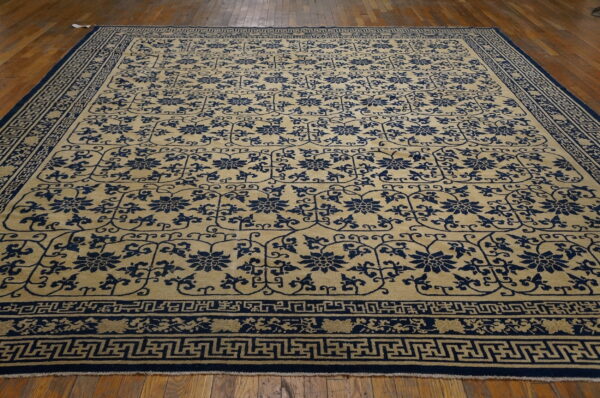 Beige rug featuring repeated navy blue floral motifs and complex geometric borders on a distressed hardwood floor.