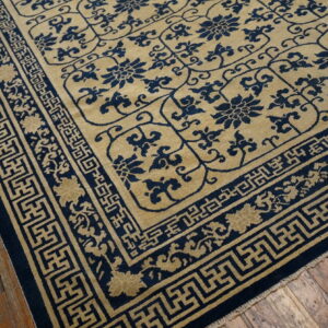 Navy blue and tan rug with floral patterns and a geometric fret border on wood planks.