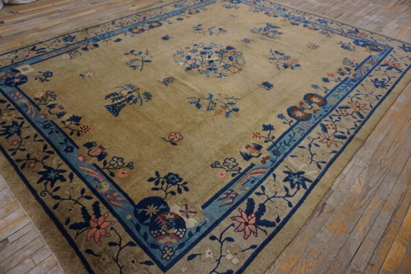 Khaki field rug with scattered blue and pink oriental floral patterns and a wide blue border.