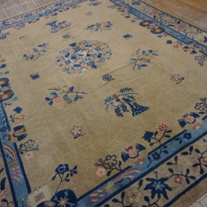 Muted beige area rug featuring navy and light blue floral patterns resting on rustic hardwood planks.