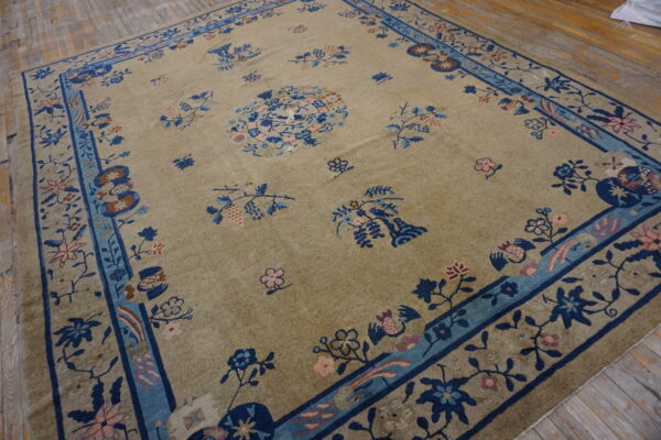 Muted beige area rug featuring navy and light blue floral patterns resting on rustic hardwood planks.