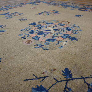Textured tan low-pile rug featuring scattered deep blue and pale pink floral designs and a medallion.