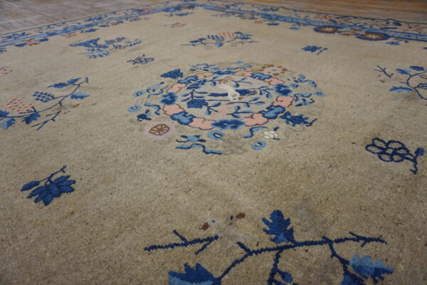 Textured tan low-pile rug featuring scattered deep blue and pale pink floral designs and a medallion.