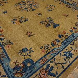 Golden-tan rug with indigo and pale blue border and scattered floral motifs rests on rustic herringbone wood flooring.