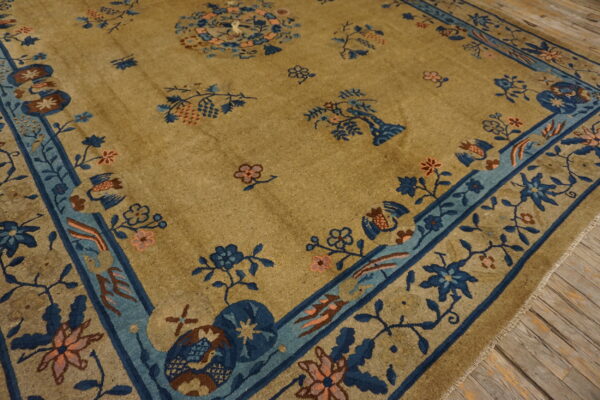 Golden-tan rug with indigo and pale blue border and scattered floral motifs rests on rustic herringbone wood flooring.