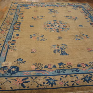 A tan rug with a navy and light blue border and scattered pink and blue floral motifs rests on a wood floor.