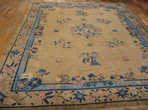 A tan rug with a navy and light blue border and scattered pink and blue floral motifs rests on a wood floor.