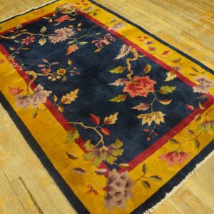 A navy blue rug with vibrant floral motifs and a thick yellow border rests on light wood plank flooring.