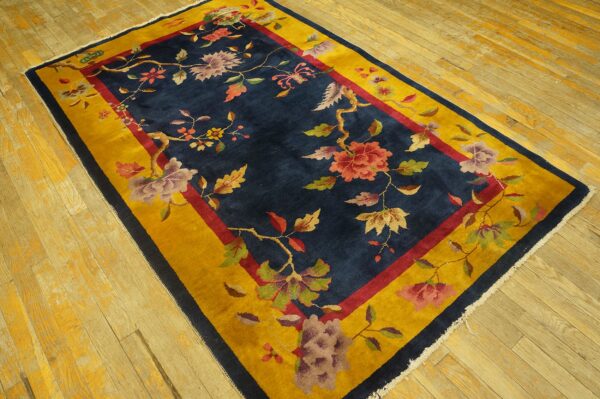 A navy blue rug with vibrant floral motifs and a thick yellow border rests on light wood plank flooring.