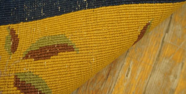 Detail shot of a flatweave rug curled on a distressed yellow floor, featuring navy, mustard, and earthy tones.