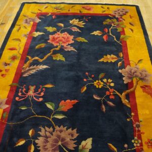 A navy blue rug features multicolored floral vines and a wide golden yellow border on distressed wood flooring.