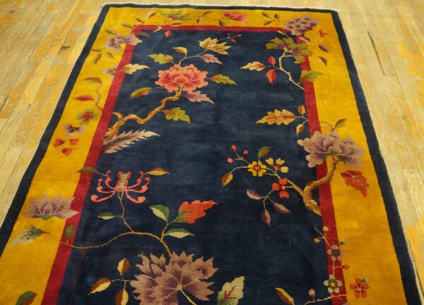 A navy blue rug features multicolored floral vines and a wide golden yellow border on distressed wood flooring.