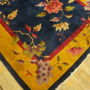 Navy blue rug corner with red and yellow borders and multicolored floral vine motifs rests on light wood planks.