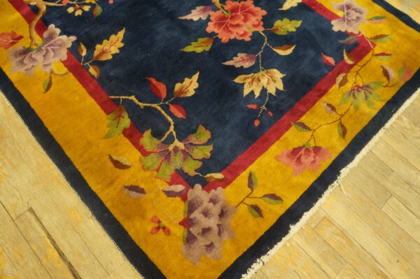 Navy blue rug corner with red and yellow borders and multicolored floral vine motifs rests on light wood planks.