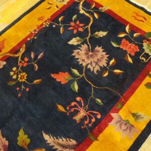 Navy floral and vine rug featuring coral and maroon colors, framed by a thick gold border on wood floor.