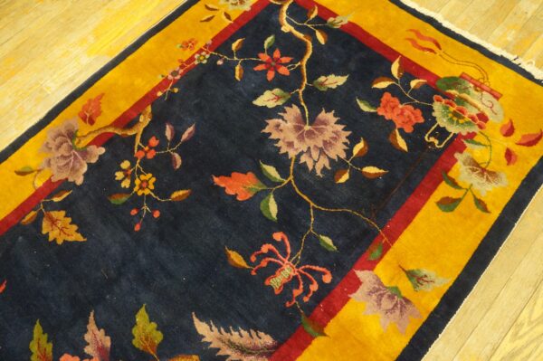 Navy floral and vine rug featuring coral and maroon colors, framed by a thick gold border on wood floor.