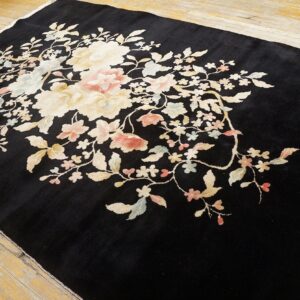Black plush rug with large cream and pale pink floral pattern lying on light wood flooring.