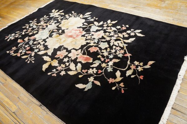 Black plush rug with large cream and pale pink floral pattern lying on light wood flooring.