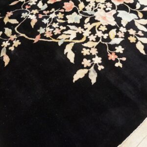 Detail of a dark high-pile rug with sprawling pastel flowers and leaves on light wood flooring.