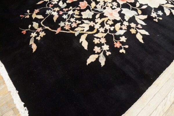 Detail of a dark high-pile rug with sprawling pastel flowers and leaves on light wood flooring.