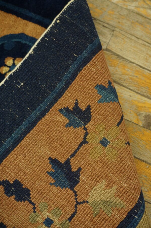 Close-up of a tightly woven blue and copper patterned rug, partially rolled on distressed yellow wooden planks.