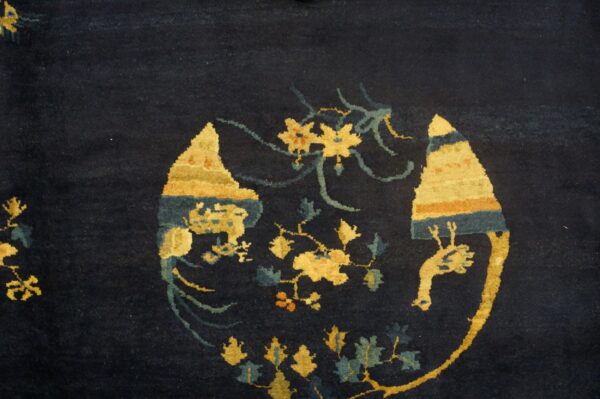 Close-up of a dark blue rug with contrasting gold, teal, and orange stylized floral and abstract motifs.