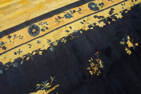Close-up of a high-pile navy blue rug featuring wide tan and gold floral borders on a wood floor.