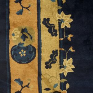 Close-up of a high-pile rug with navy blue and gold floral borders on light wood planks.