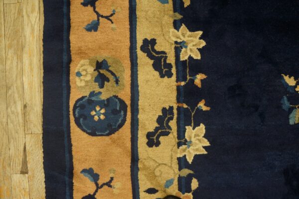 Close-up of a high-pile rug with navy blue and gold floral borders on light wood planks.