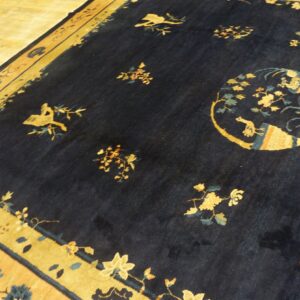 Navy blue rug featuring gold and teal scattered floral patterns and wide borders on light wood flooring.