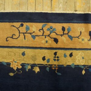 High-pile rug border in navy and tan with blue floral vines rests on wide, distressed wood floorboards.