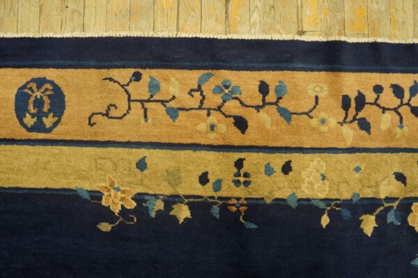 High-pile rug border in navy and tan with blue floral vines rests on wide, distressed wood floorboards.