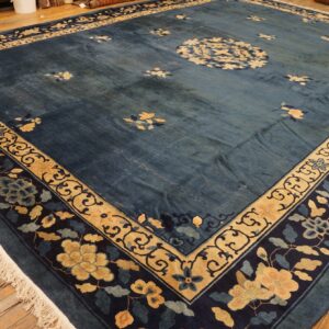 Deep blue rug with gold and navy floral borders and light floral sprays covers wood flooring.
