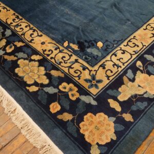 Deep blue rug with elaborate tan and navy floral borders rests on distressed wooden planks.