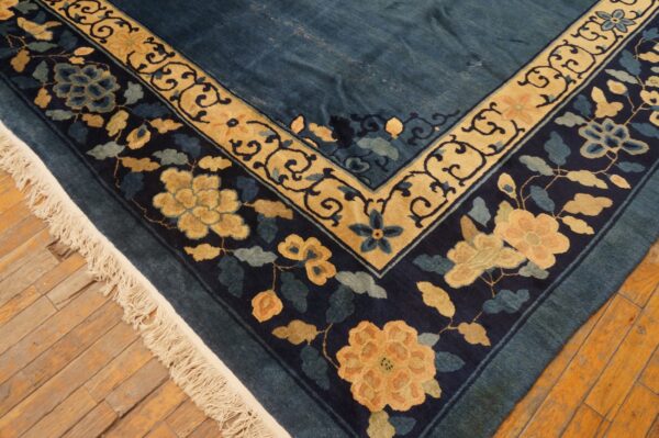 Deep blue rug with elaborate tan and navy floral borders rests on distressed wooden planks.