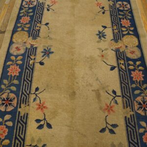 Tan runner rug featuring wide blue borders with floral and geometric designs rests on distressed wood flooring.