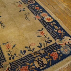 A tan rug with a navy blue border featuring coral flowers and a geometric pattern lies on wood floors.